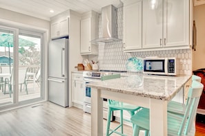 A modern kitchen with white cabinets, a stainless steel refrigerator, a microwave, and a large island with bar stools. - Sunny, dog-friendly beach house with a washer/dryer, central AC, & deck (North Myrtle Beach)