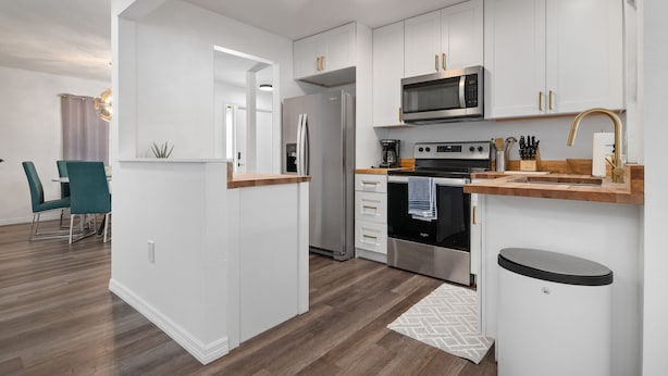 A modern kitchen with white cabinets, stainless steel appliances, and a wooden countertop.