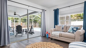 A living room with a sliding glass door leading to a patio area, a beige sofa, and a woven rug.