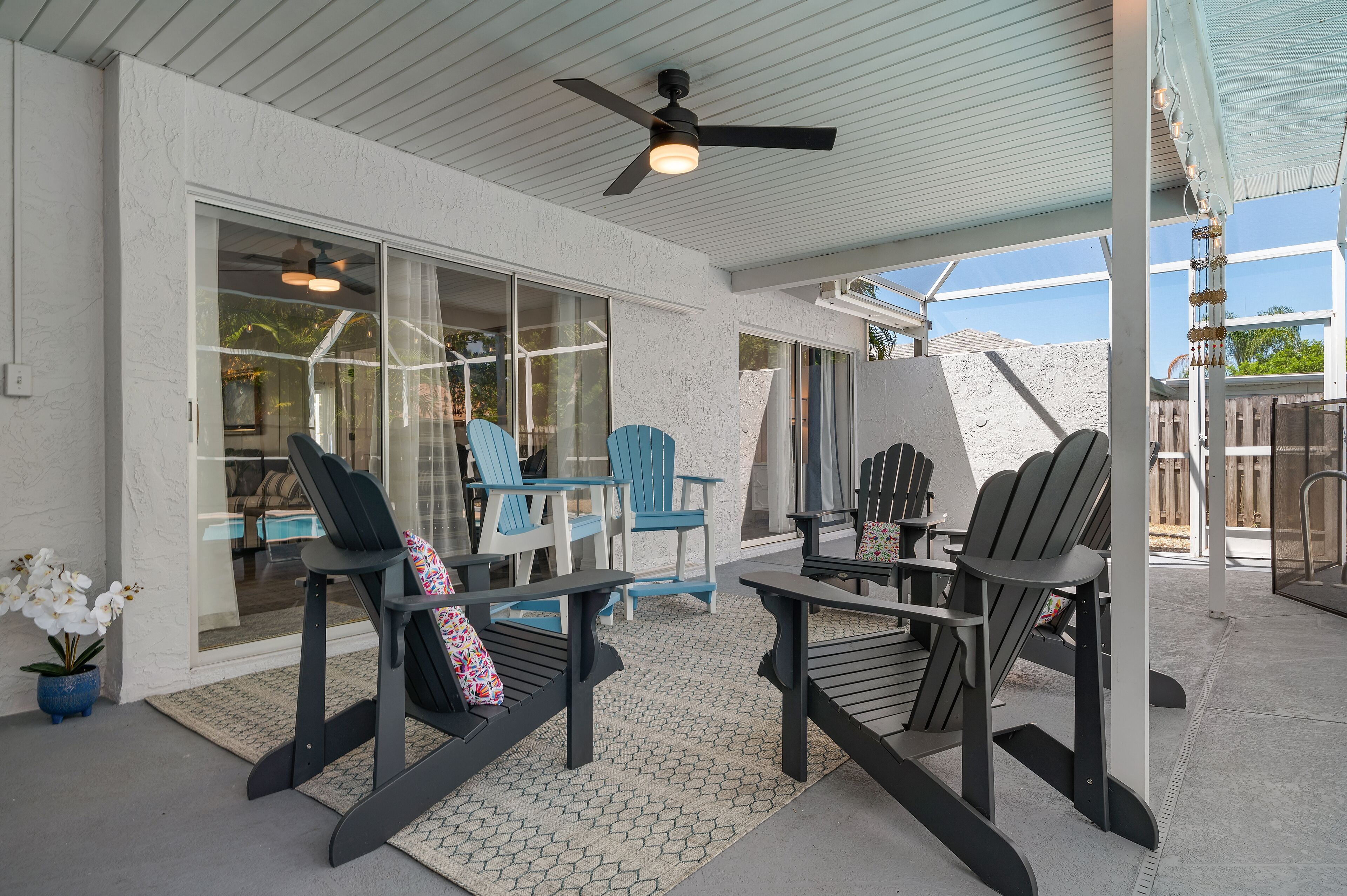 A covered patio area with Adirondack chairs, a table, and a ceiling fan.