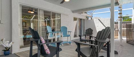A covered patio area with Adirondack chairs, a table, and a ceiling fan.