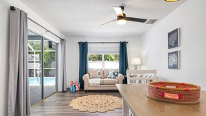 A living room with a sofa, a coffee table, a ceiling fan, and a large window with curtains.