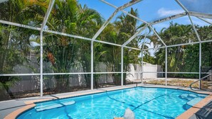 A swimming pool with a clear blue water, surrounded by a white fence and lush greenery.
