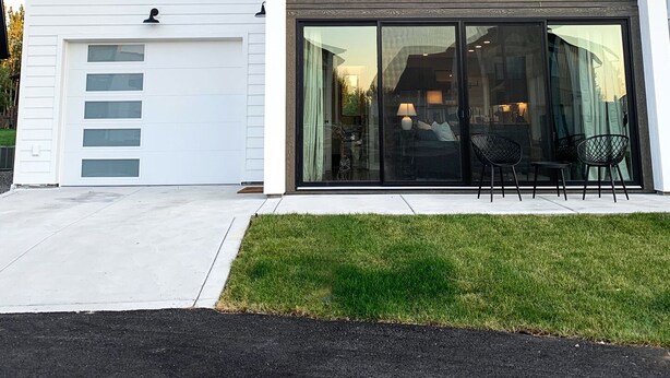 Una casa moderna de dues plantes amb un garatge blanc i grans portes corredisses de vidre que donen a un pati amb mobiliari exterior.