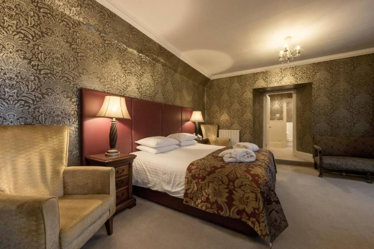 A hotel room with a large bed, two bedside lamps, a nightstand, a chair, and a door leading to another room.