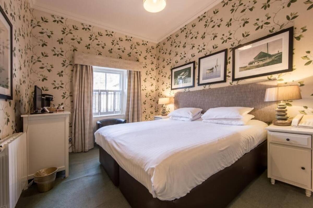 A hotel room with a large bed, bedside tables, a dresser, a window with curtains, and framed pictures on the wall.
