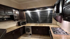 A kitchen with dark cabinets, a stainless steel range hood, a built-in washer, and a granite countertop.