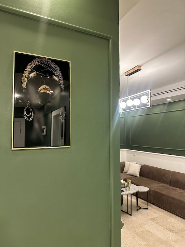 A room with a green wall, a mirror, a brown sofa, a small round table, and a ceiling light fixture.