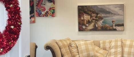 A living room with a beige sofa, a glass coffee table, and a red tinsel wreath on the door.