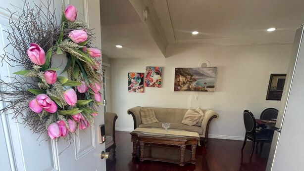 Een gang met een houten vloer, een beige bank, een bijzettafeltje en een decoratieve bloemstelling bij de deur.