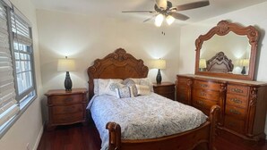 Een slaapkamer met een houten bed, twee nachtkastjes met lampen, een plafondventilator, een grote spiegel en een dressoir.