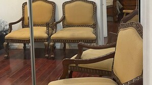 Een kamer met twee sierlijke houten stoelen met beklede zittingen en rugleuningen, een houten vloer en een glazen scheidingswand.