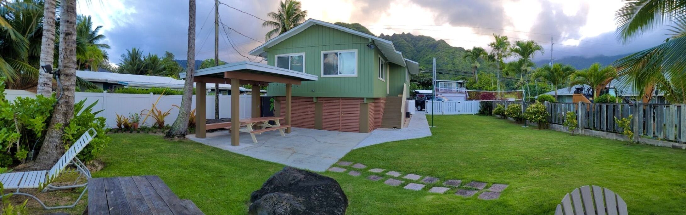 A green house with a covered patio and a stone pathway leading to the entrance.