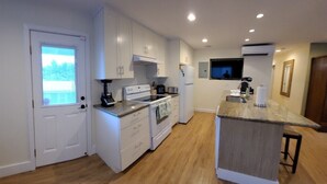A modern kitchen with white cabinets, a built-in oven, a coffee machine, and a TV mounted above the counter. - Modern Oceanfront North Shore House, w/ AC & volleyball net, near Kualoa Ranch (Hauula)