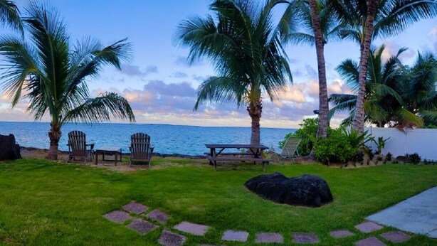 A backyard with a view of the ocean, palm trees, a wooden fence, and a picnic table. - Modern Oceanfront North Shore House, w/ AC & volleyball net, near Kualoa Ranch (Hauula)