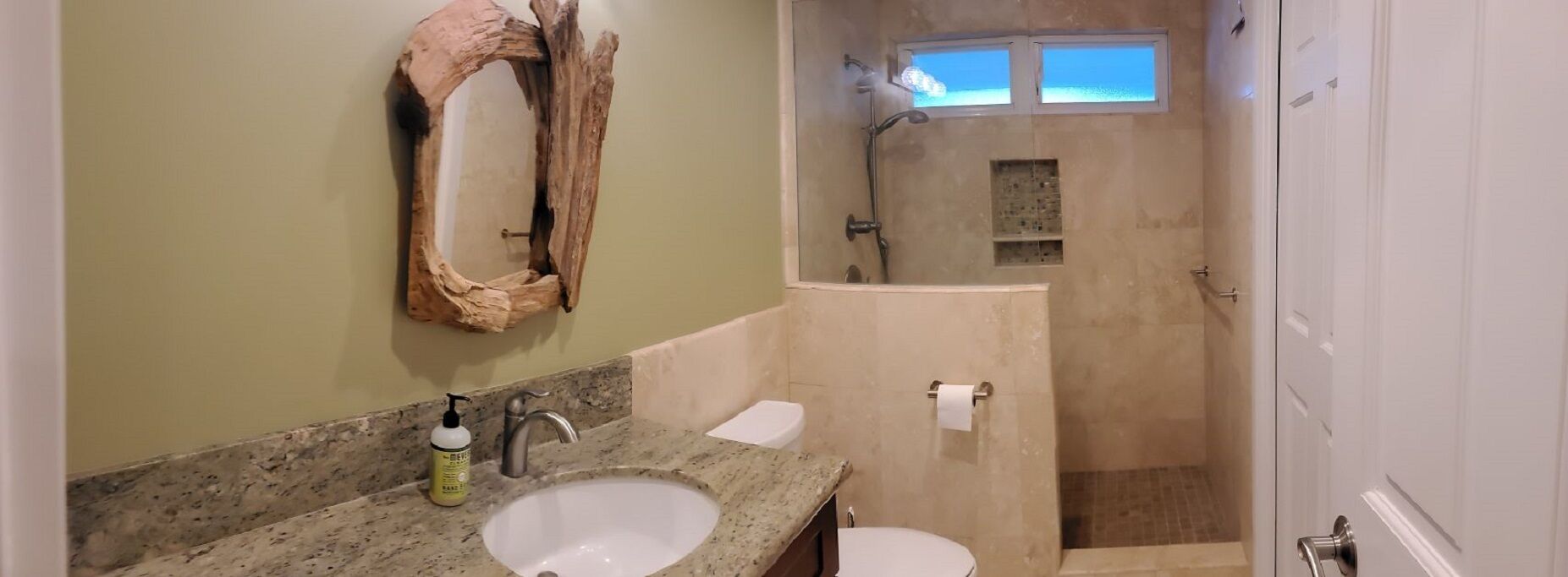 A bathroom with a granite countertop, a white sink, a wooden mirror, a shower with a glass door, and a toilet.