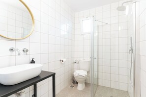 A modern bathroom with a white sink, toilet, and glass shower enclosure. - Selina Kinneret (Migdal)