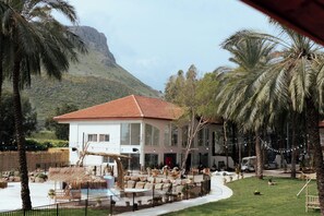 A resort with a white building, a pool, and palm trees. - Selina Kinneret (Migdal)