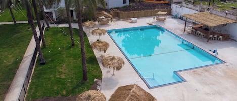 Una piscina con un deck circundante, palmeras y sombrillas de paja.