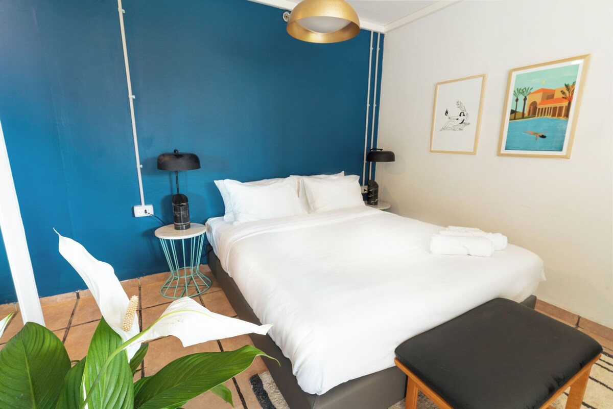 A hotel room with a large bed, a small round table, a lamp, and a wall with two framed pictures.