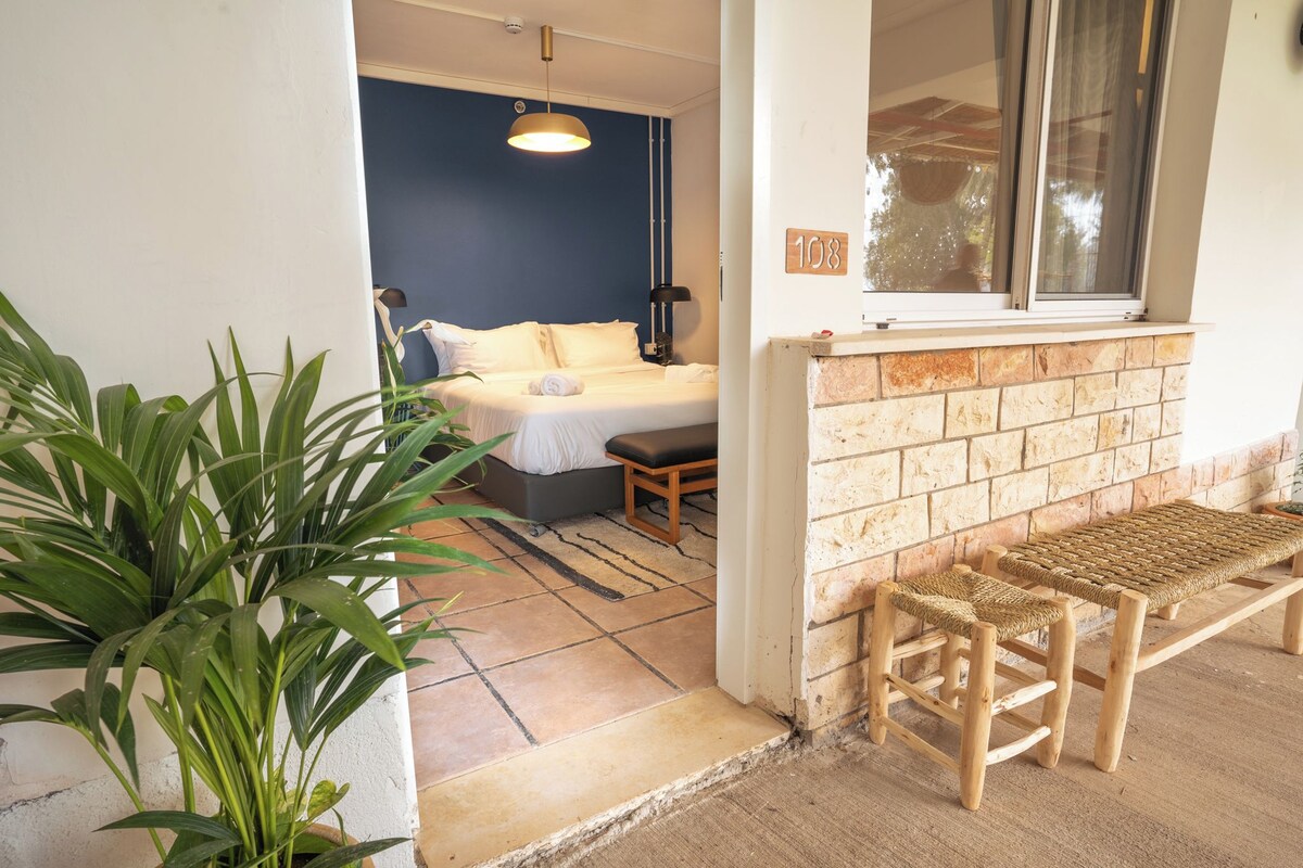 A room with a bed, a bench, and a window overlooking a brick wall.
