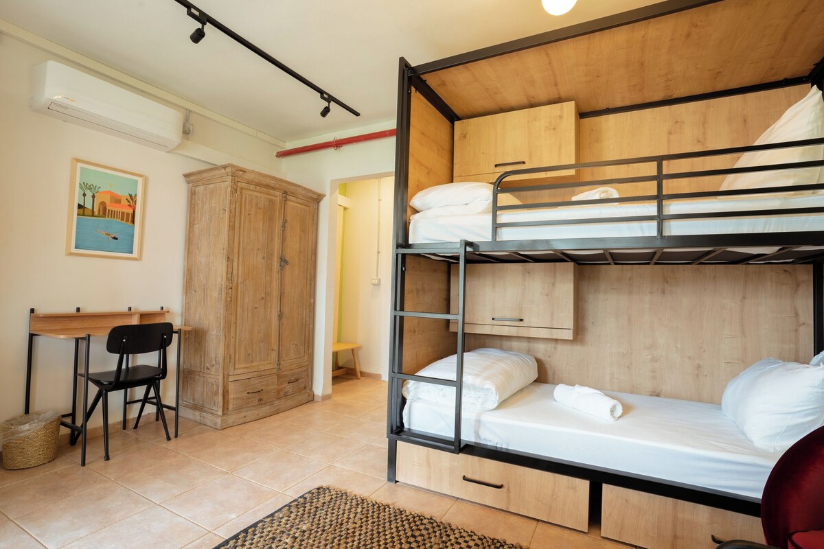 A bunk bed room with a desk and chair, wooden wardrobe, and a painting on the wall.