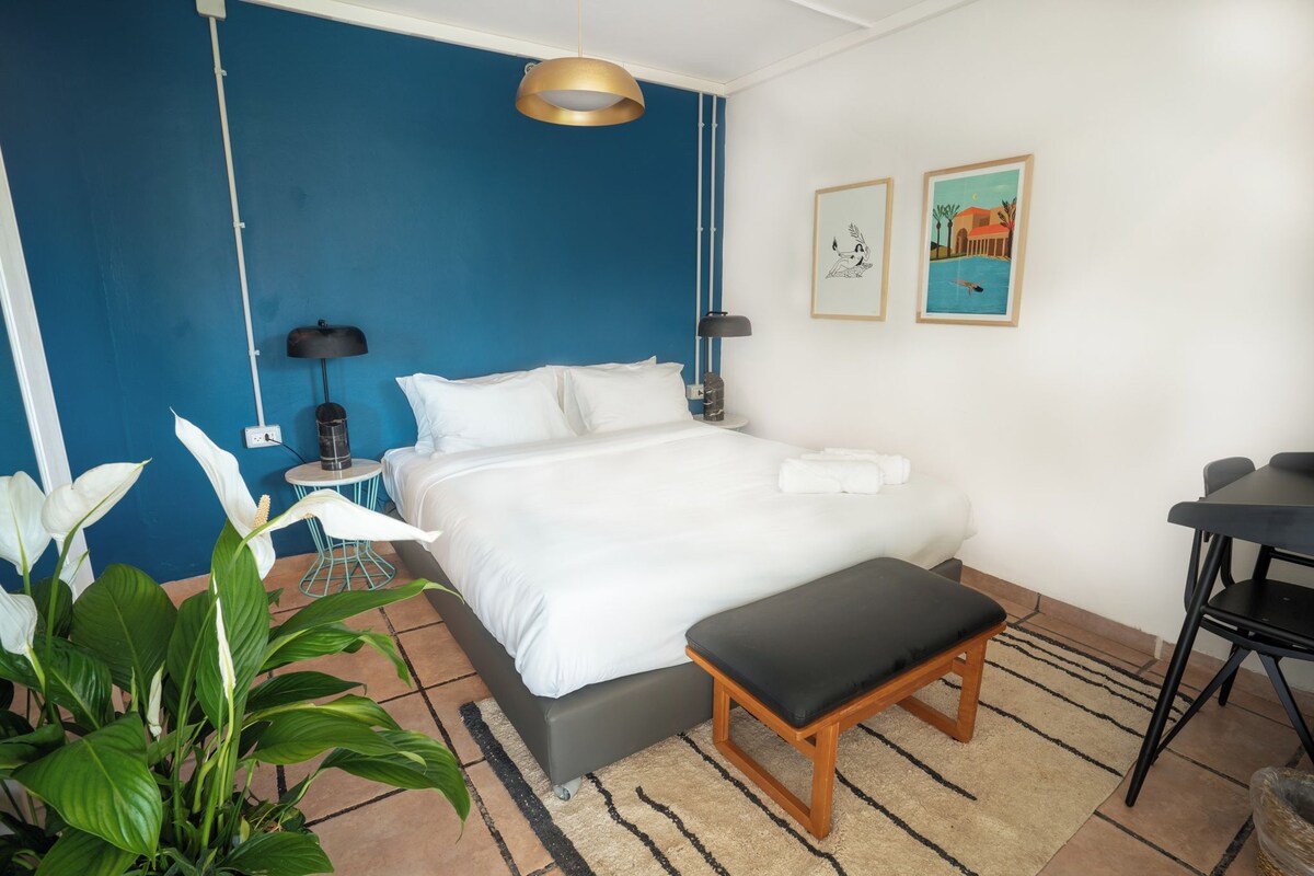 Une chambre d’hôtel comprenant un lit, une table de chevet, une lampe, une œuvre d’art et une petite table avec des chaises.
