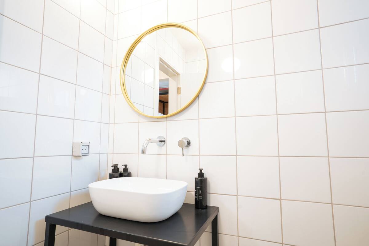 A modern bathroom with a white sink, black countertop, and a gold-framed mirror.