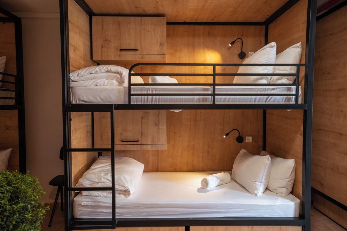 A bunk bed room with a wooden headboard, a bedside table, and a wall-mounted lamp.