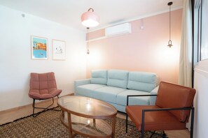 A modern living room with a light blue sofa, two brown chairs, a glass coffee table, and a pink pendant light. - Selina Kinneret (Migdal)