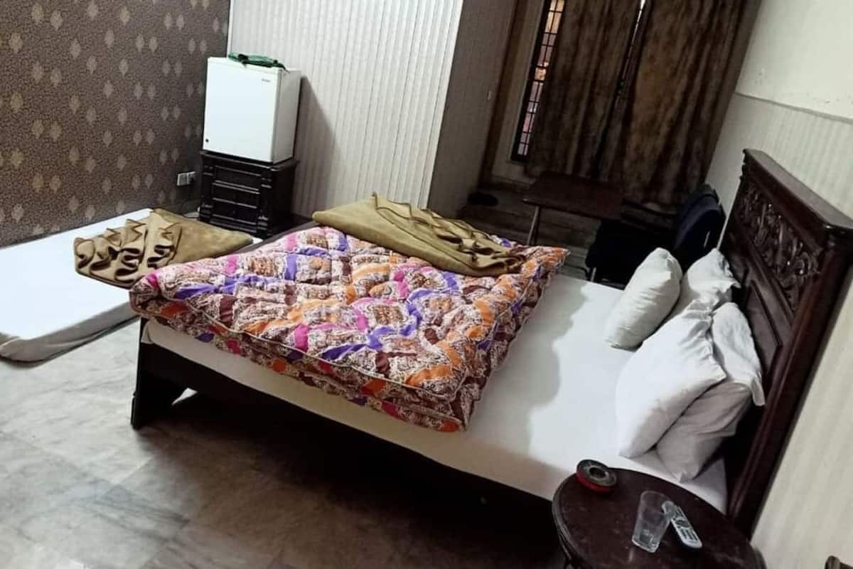 Une chambre à coucher avec un lit, des oreillers, une table de chevet, une petite table sur laquelle se trouve une bouteille, et un radiateur fixé au mur.