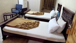 Two single beds with wooden headboards, a small round table, a blue chair, and a white wall. - Hotel Al Hateem Palace (Mekhtar)