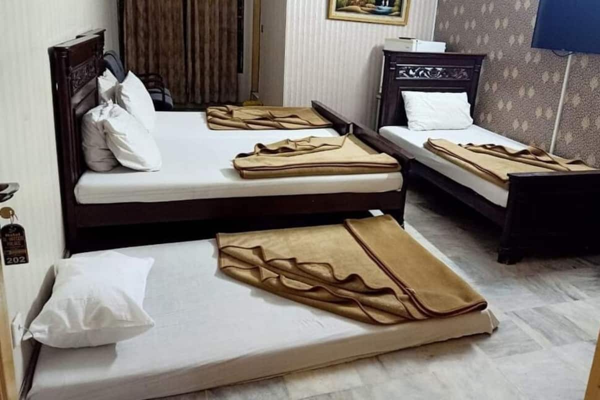Une chambre d’hôtel avec trois lits simples, chacun étant équipé d’un oreiller blanc et d’une couverture marron.