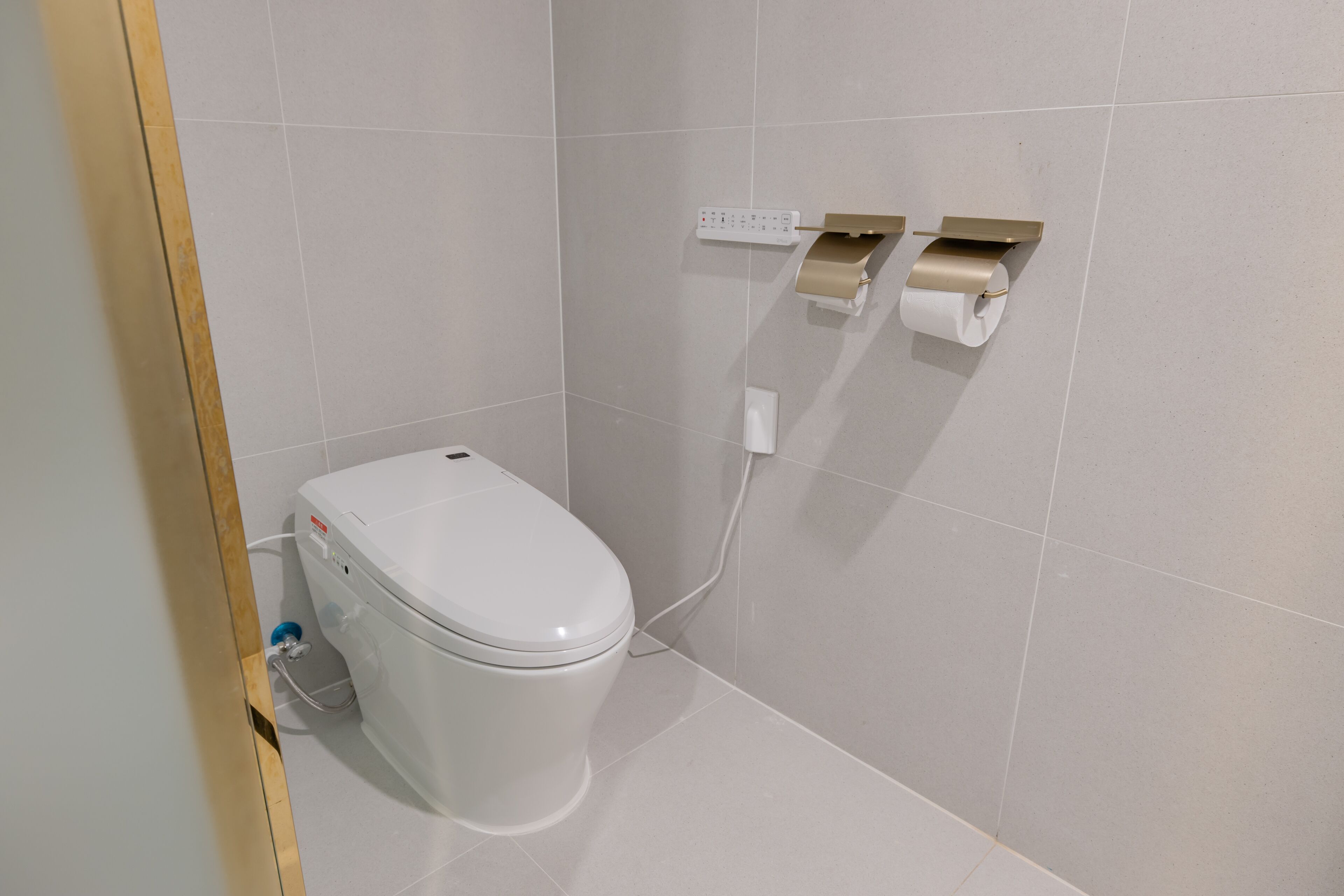 A modern bathroom with a toilet, a wall-mounted paper dispenser, and a power outlet.