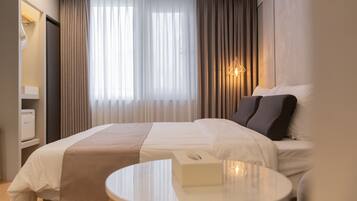 A hotel room with a bed, a bedside table, a lamp, and a window with curtains.