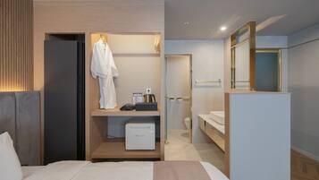 A modern hotel room with a bed, a built-in wardrobe, a small kitchenette, and a bathroom with a toilet and sink.