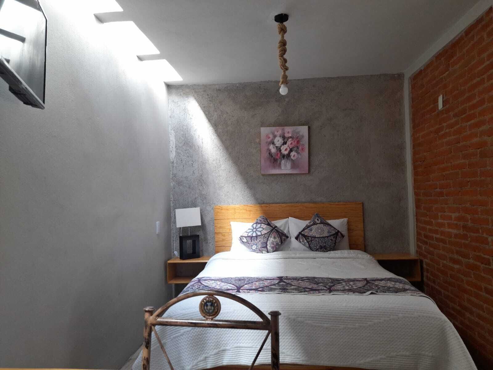 Un dormitorio con cama, mesita de noche, lámpara, un cuadro y una lámpara colgante.