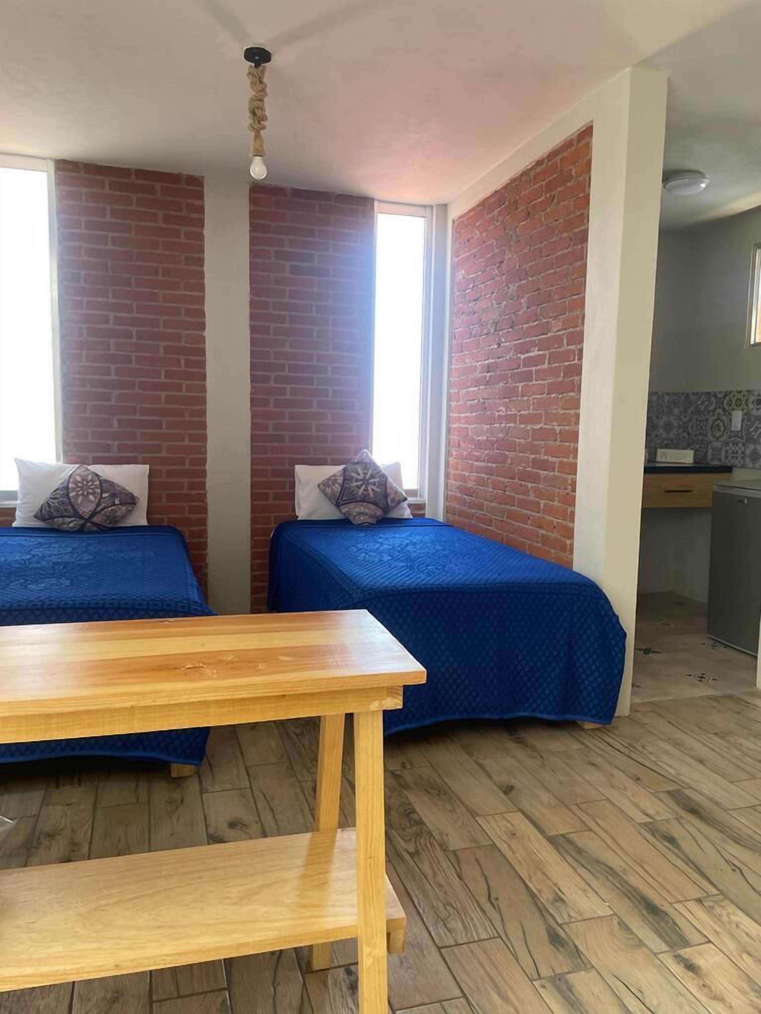 Una habitación con dos camas, una mesa de madera y una pared de ladrillo.