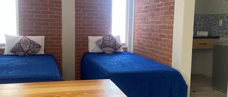 Una habitación con dos camas, una mesa de madera y una pared de ladrillo.