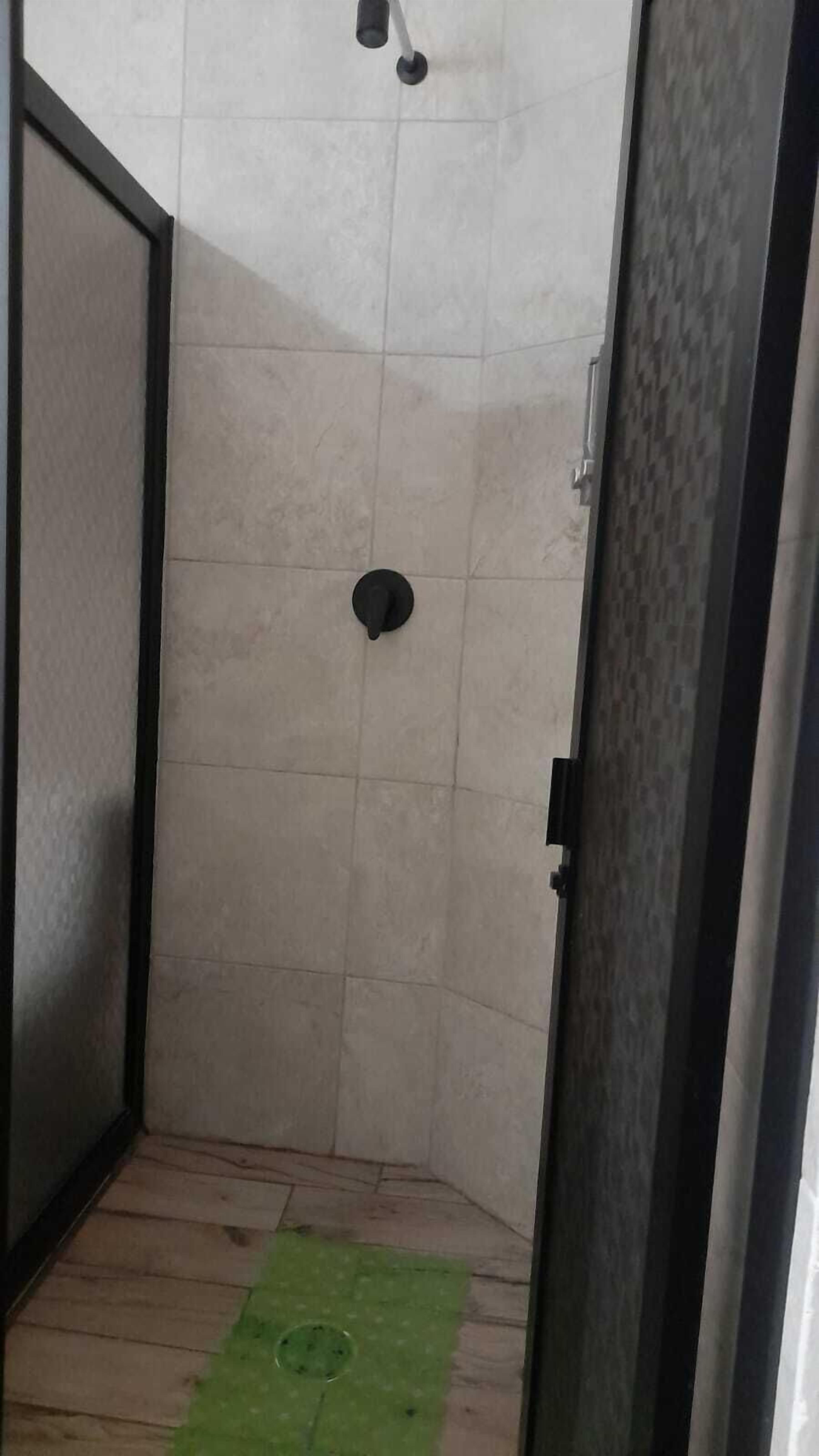 A small, tiled shower room with a green mat on the floor.