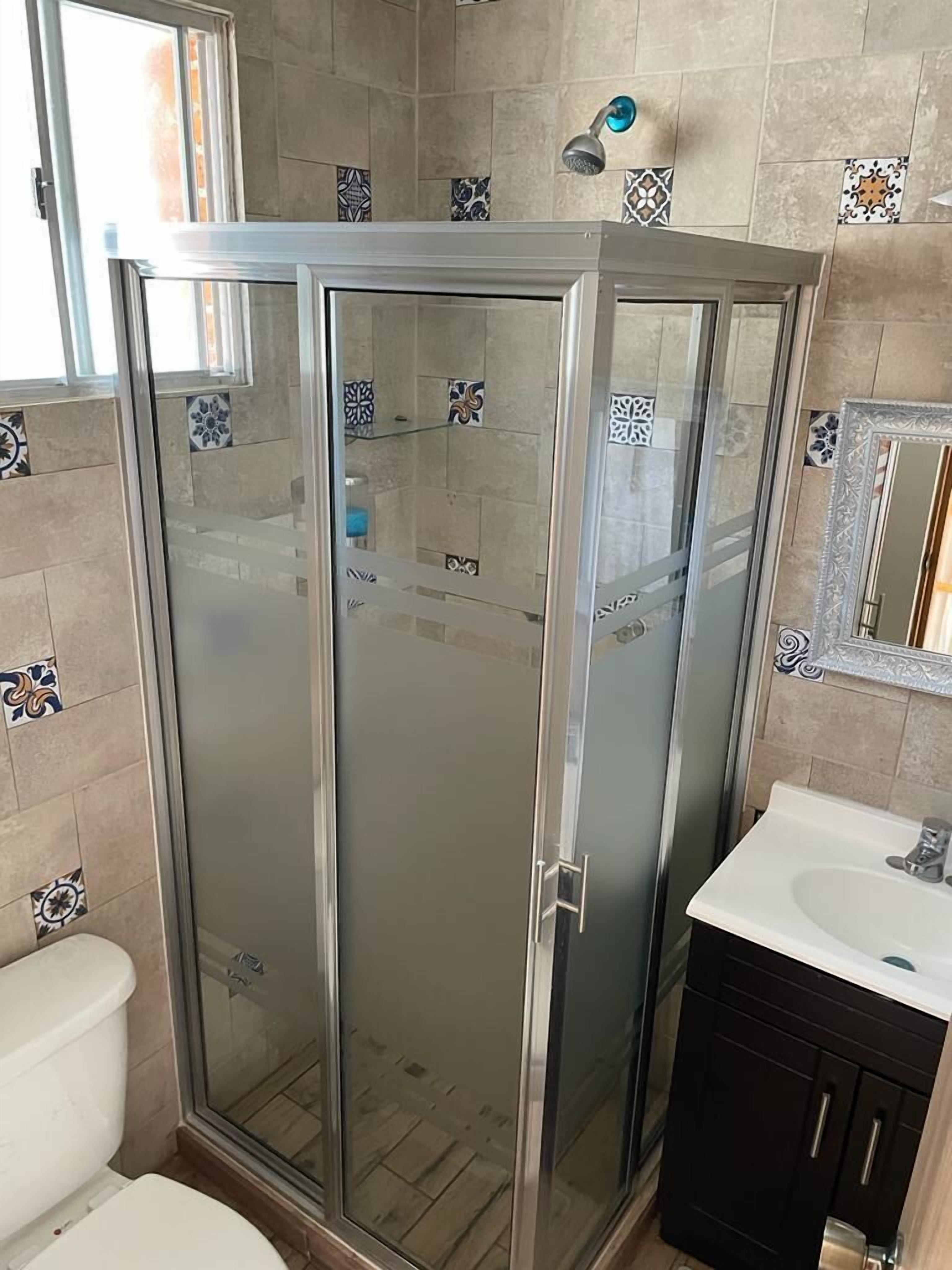 Un baño con ducha envuelta en vidrio, inodoro blanco y lavamanos con espejo arriba.