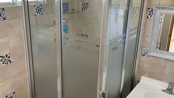 Un baño con ducha envuelta en vidrio, inodoro blanco y lavamanos con espejo arriba.