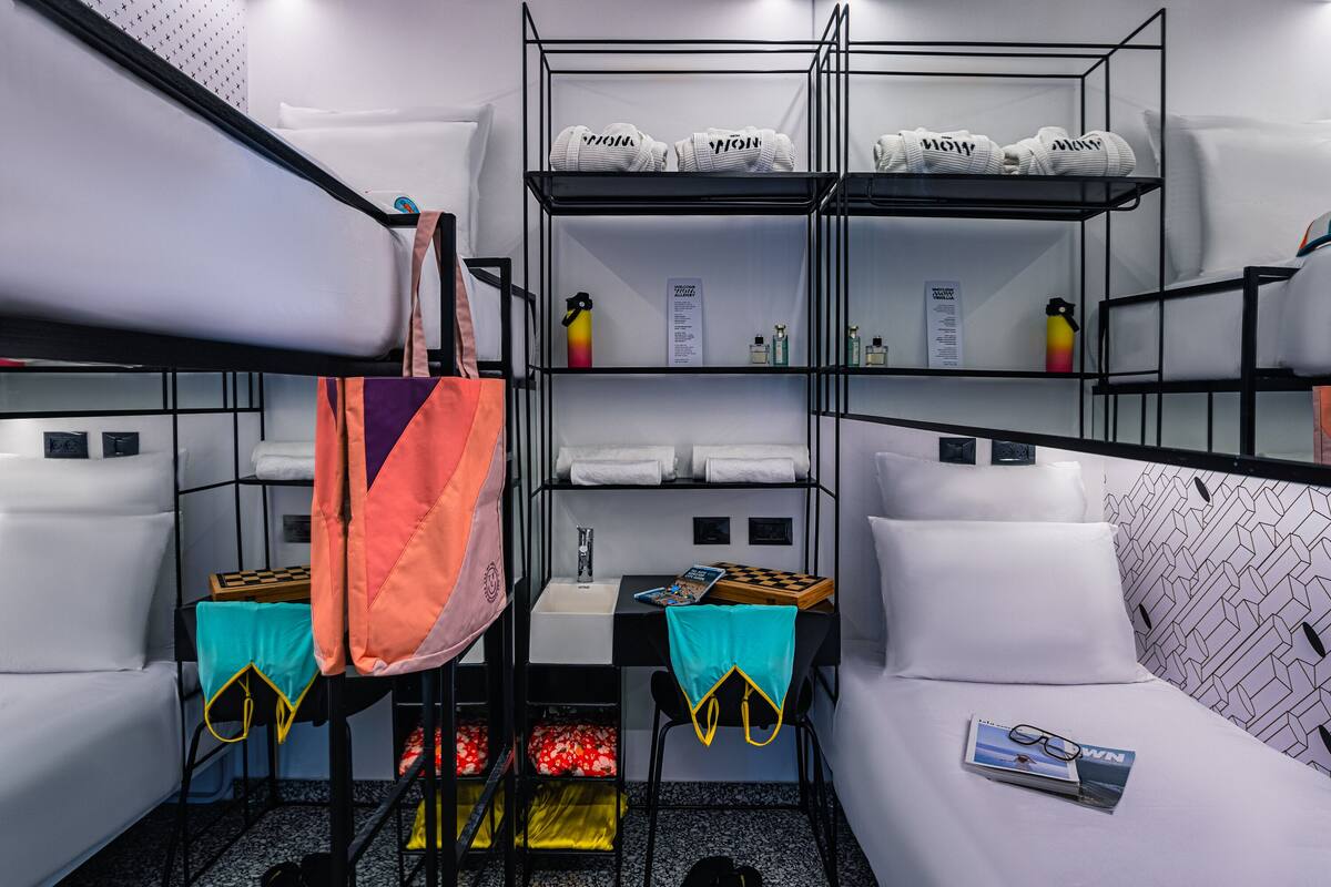 Ein kompaktes Hotelzimmer mit Stockbetten, einem kleinen Schreibtisch mit Stuhl, einem Nachttisch und einem Einzelbett.
