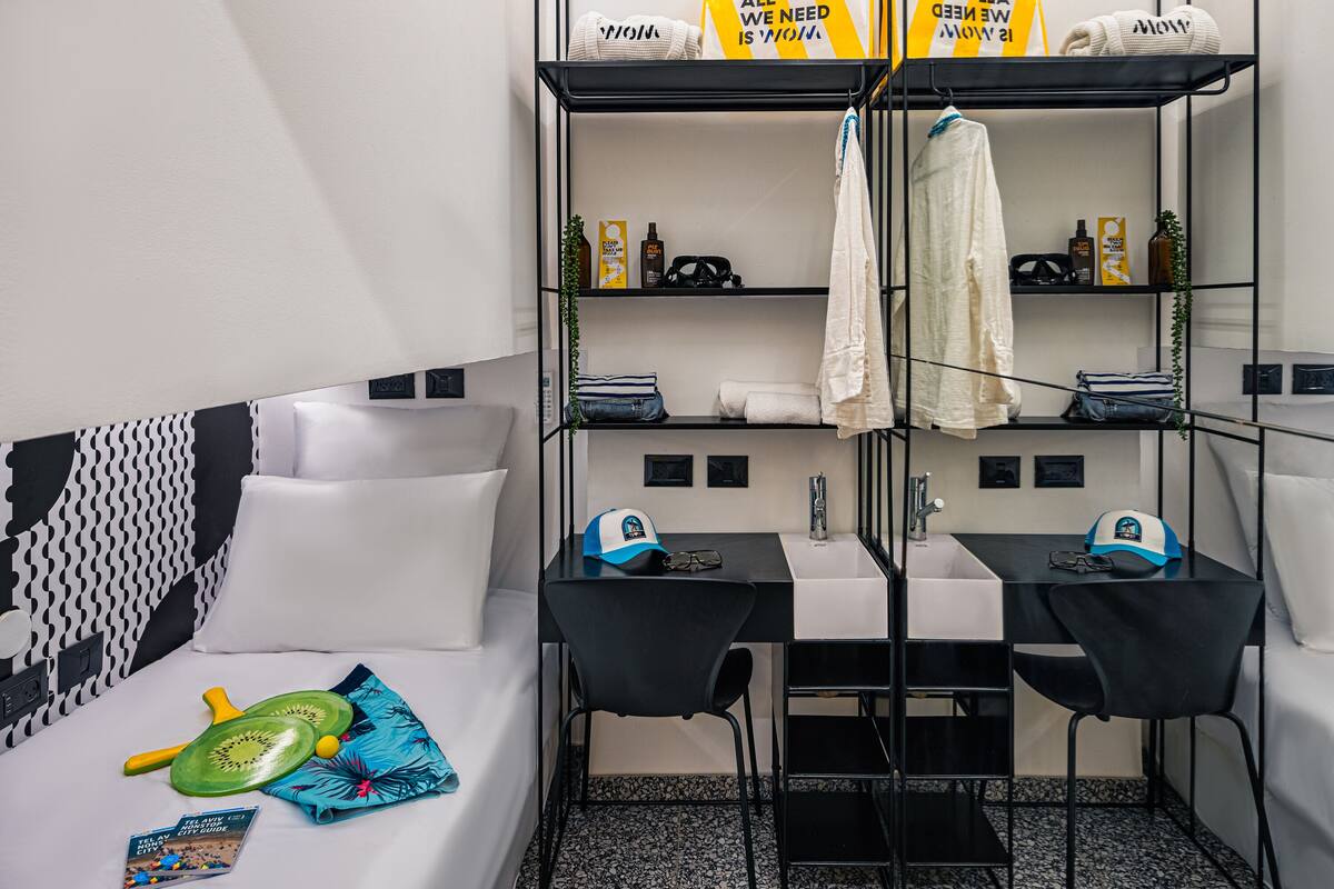 Ein kompaktes Hotelzimmer mit einem Bett, zwei schwarzen Tischen, einem Spiegel, einem Ablagefach für Toilettenartikel und einer kleinen Pflanze.