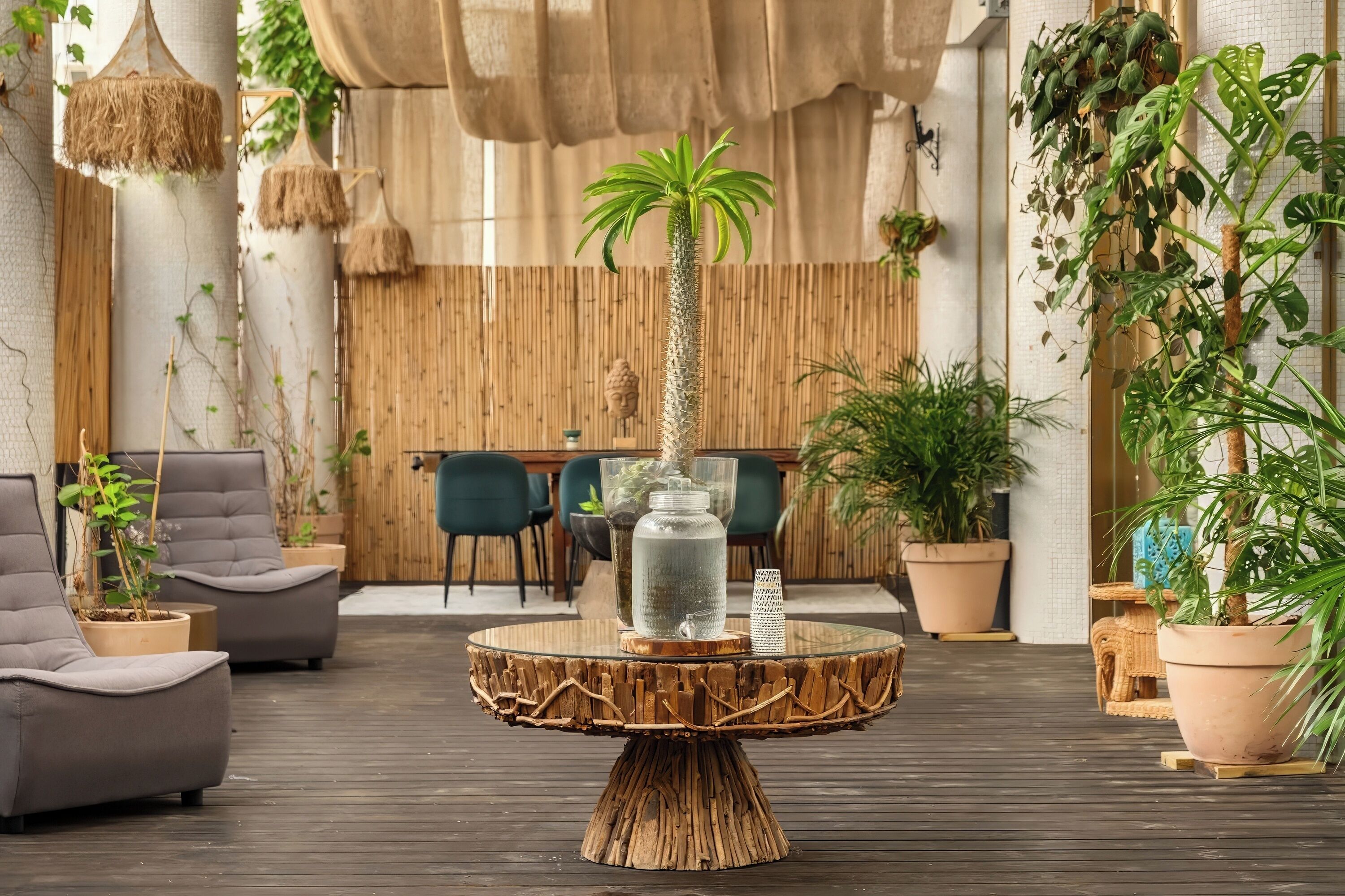 A modern lounge area with a round wooden coffee table, grey sofas, and various potted plants.