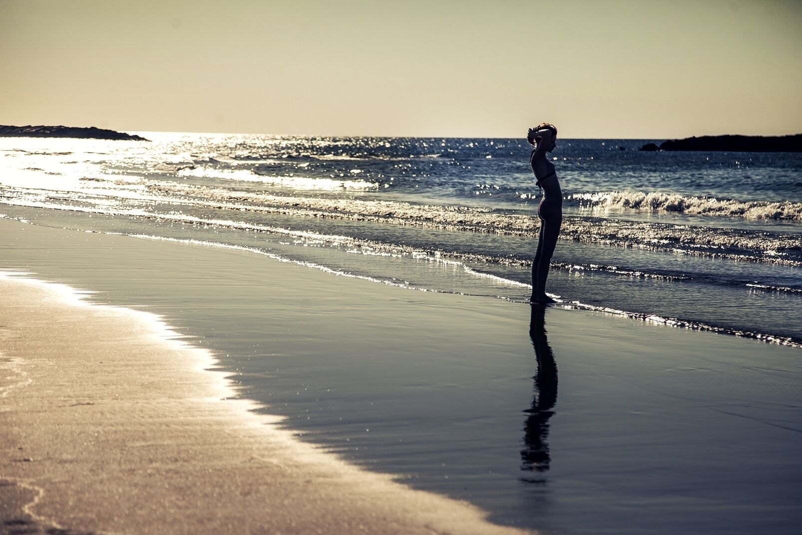 A beach scene with a person standing on the sand near the water.