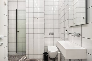 A modern bathroom with white tiles, a glass shower enclosure, a white sink, and a toilet. - WOM Beach Pod Hotel  (Tel Aviv)