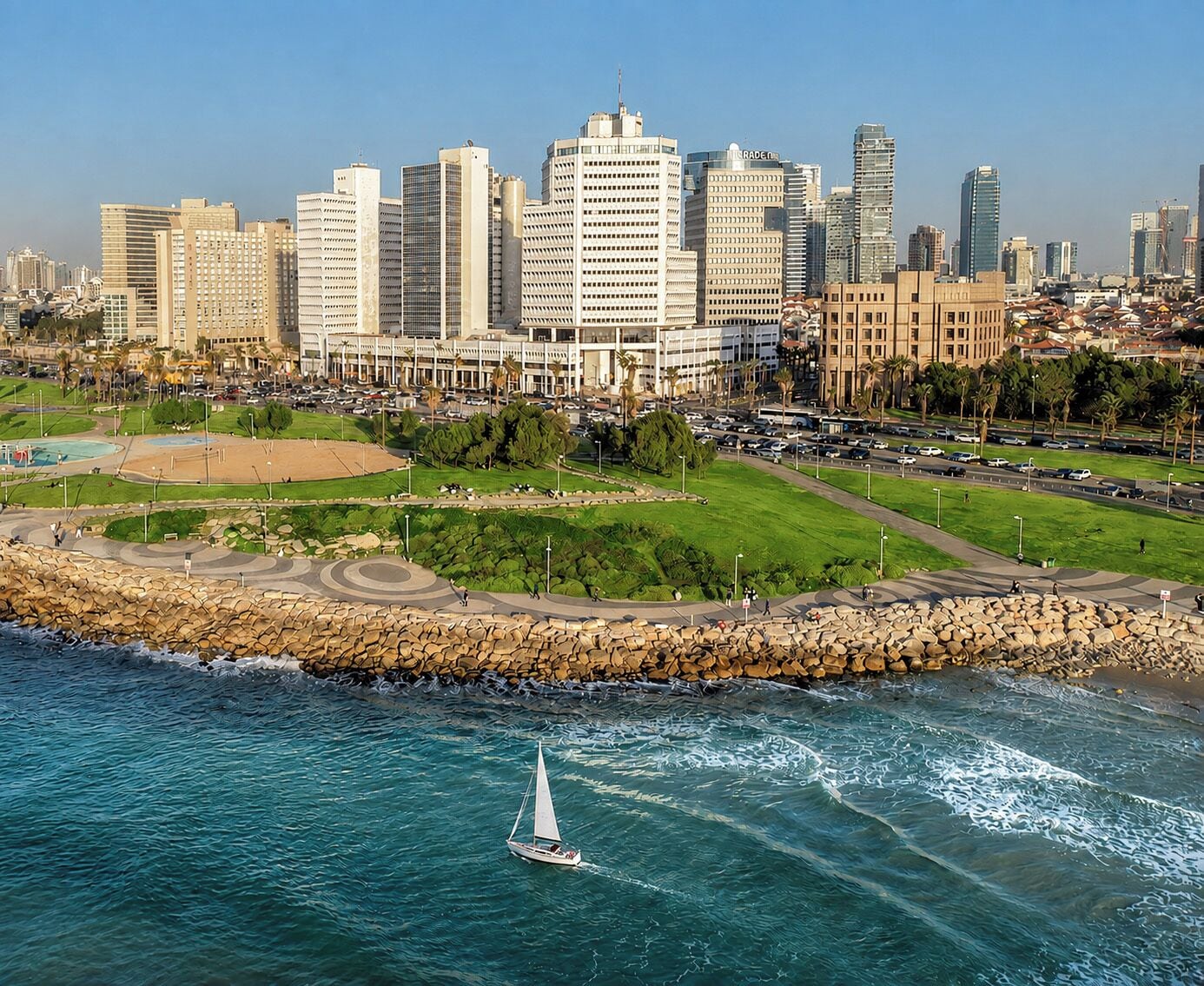Un paisaje urbano costero con un velero en el agua, un rompeolas rocoso y un horizonte urbano denso.