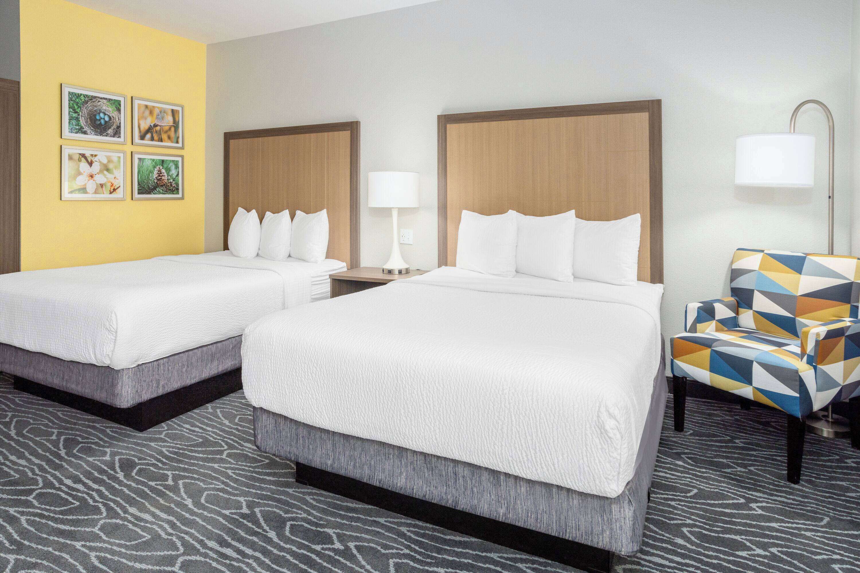A hotel room with two beds, a patterned carpet, and a colorful armchair.