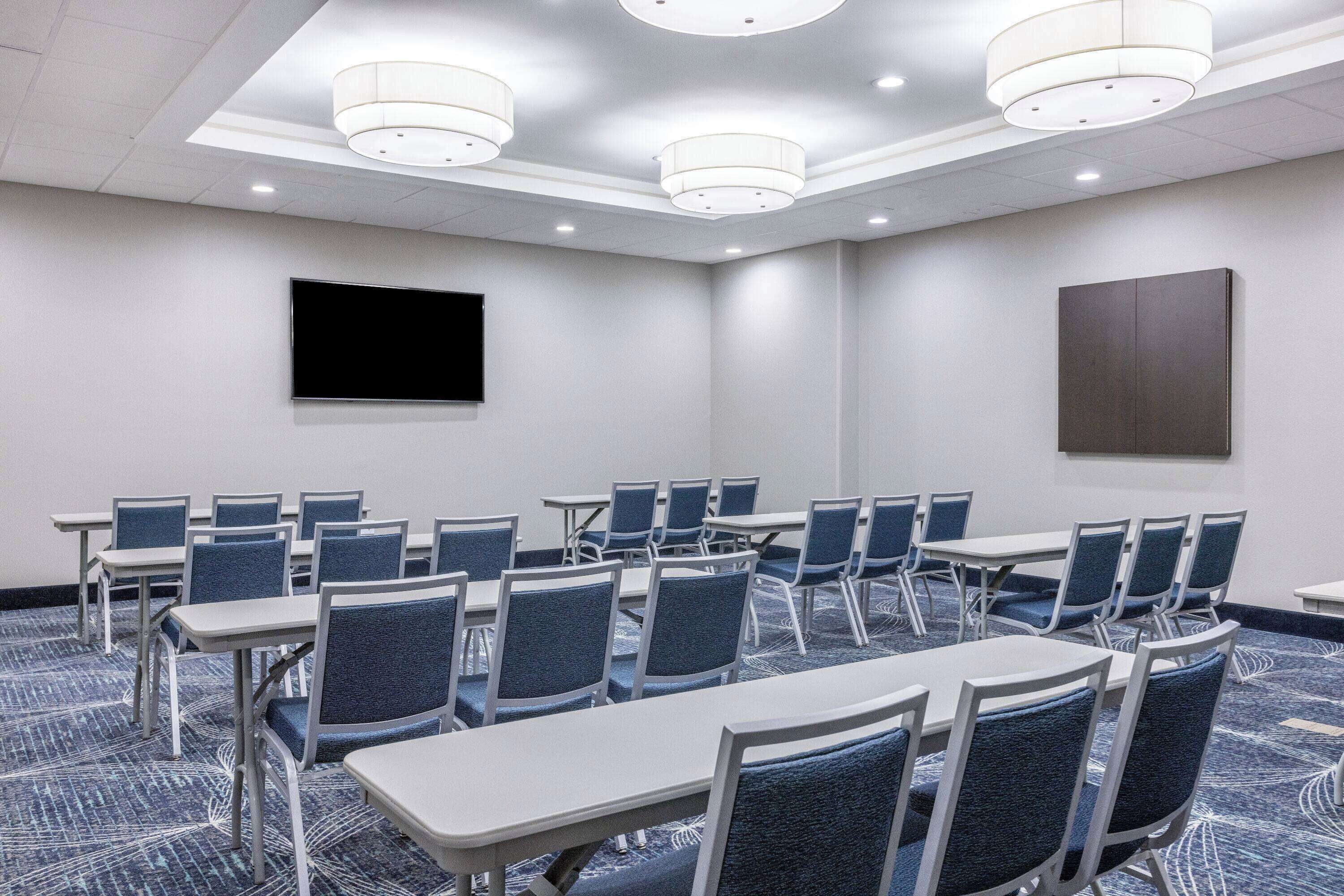 Una sala conferenze con tavoli e sedie, una TV a schermo piatto e un grande quadro appeso al muro.